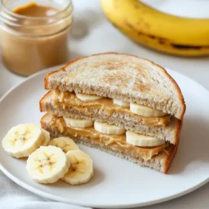 Grilled peanut butter banana sandwich with golden brown crust, melted peanut butter, and banana slices, served on a wooden plate with honey and cinnamon.