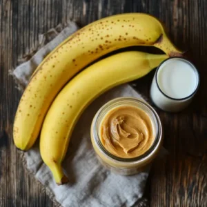 Fresh bananas, a jar of peanut butter, and a glass of milk on a wooden table.